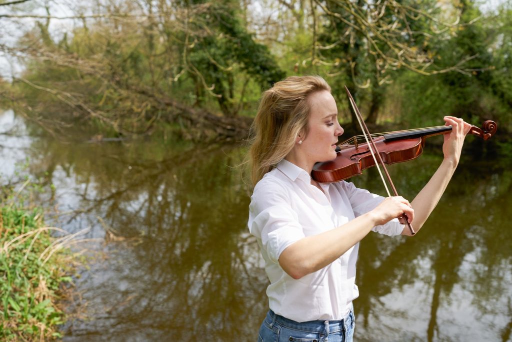 May Robertson playing the baroque violin outdoors wearing a white shirt