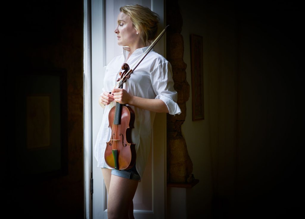 Violinist May Robertson standing by a window holding her baroque violin